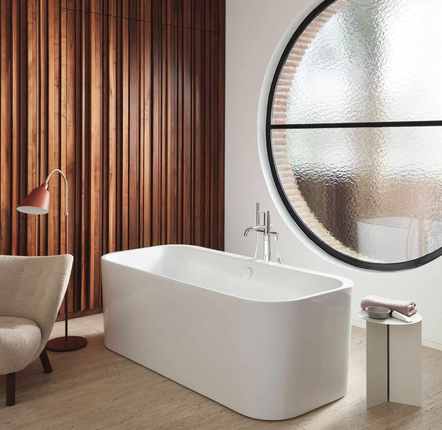 Duravit Happy D.2 Plus C-Shaped bathroom range. Freestanding bathtub in front of a large circular window.