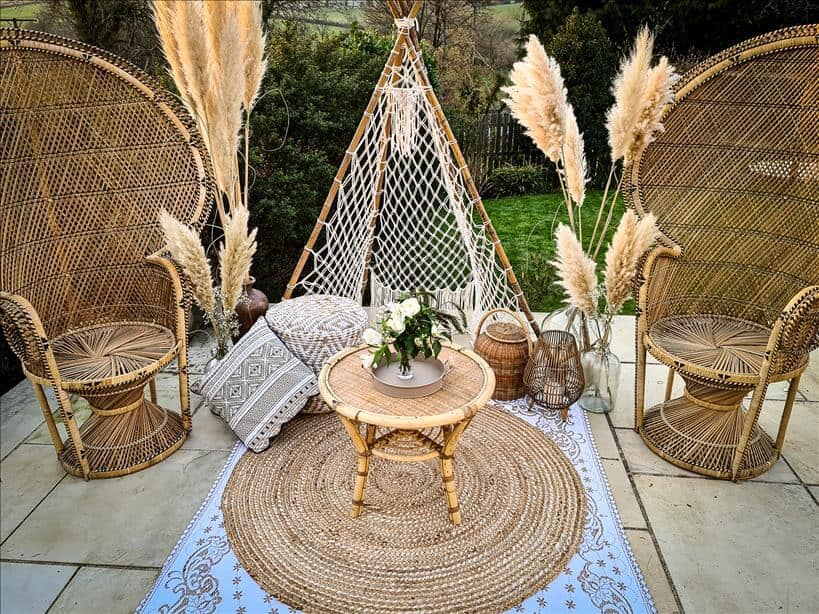 Entertain outdoors with two peacock chairs set up surrounded by large vases full of pampas grass, lanterns, pouffes and a macrame tipi