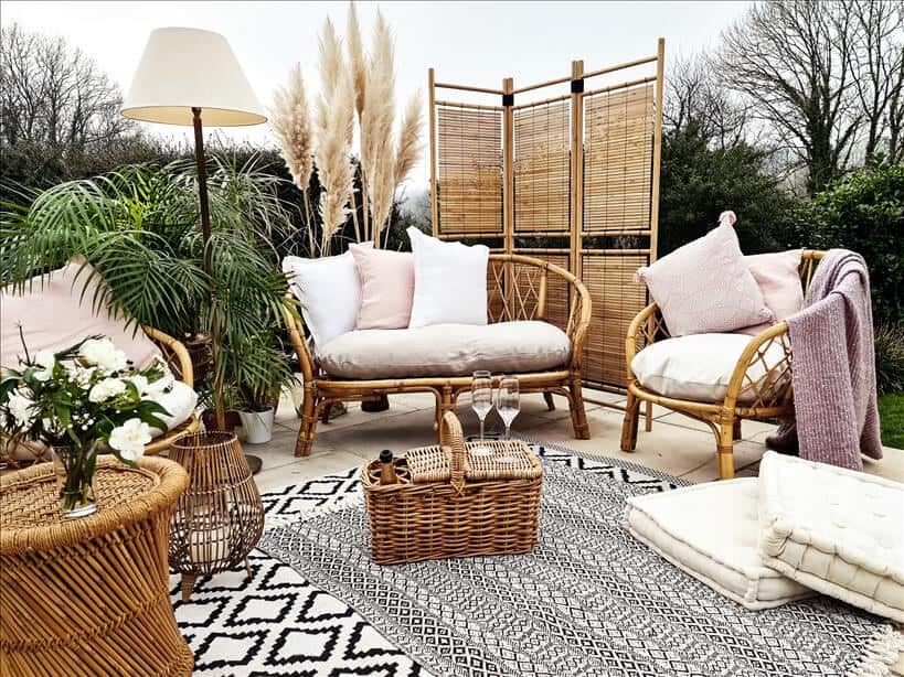 Entertain outdoors by setting up an outdoor living room. Use rattan furniture, rugs, cushions, blankets, a coffee table, side table, a lamp, and a wooden screen.