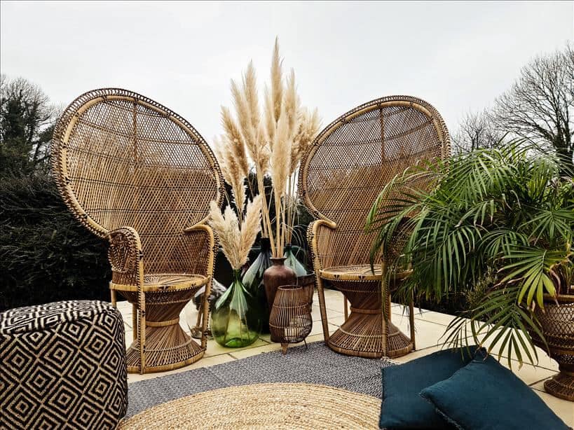 Entertain outdoors with two peacock chairs set up on rugs surrounded by large vases full of pampas grass