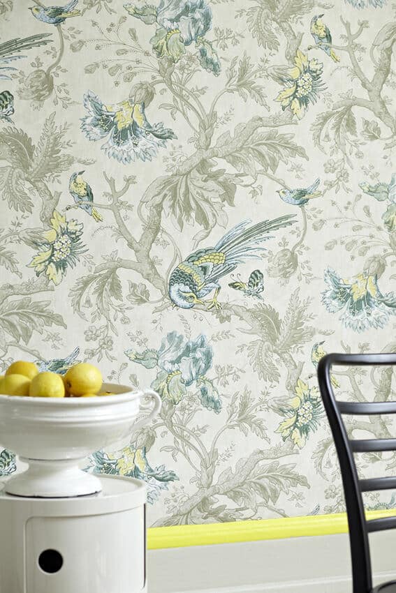 A wallpapered wall featuring birds and butterflies. The white skirting board has a neon yellow stripe at the top. Image c/o Little Greene