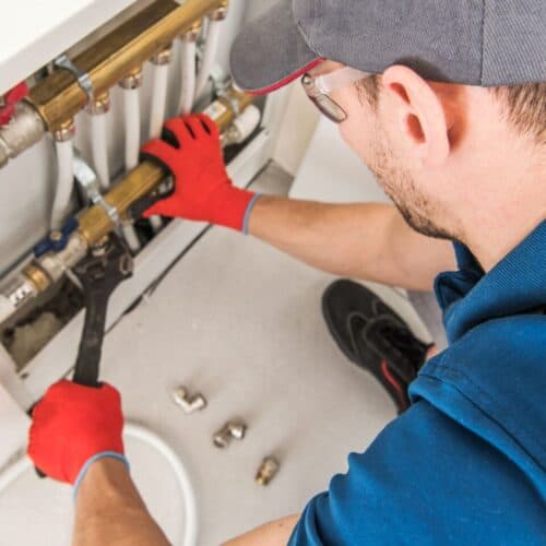 A plumber in blue overalls fixing pipes in a wall