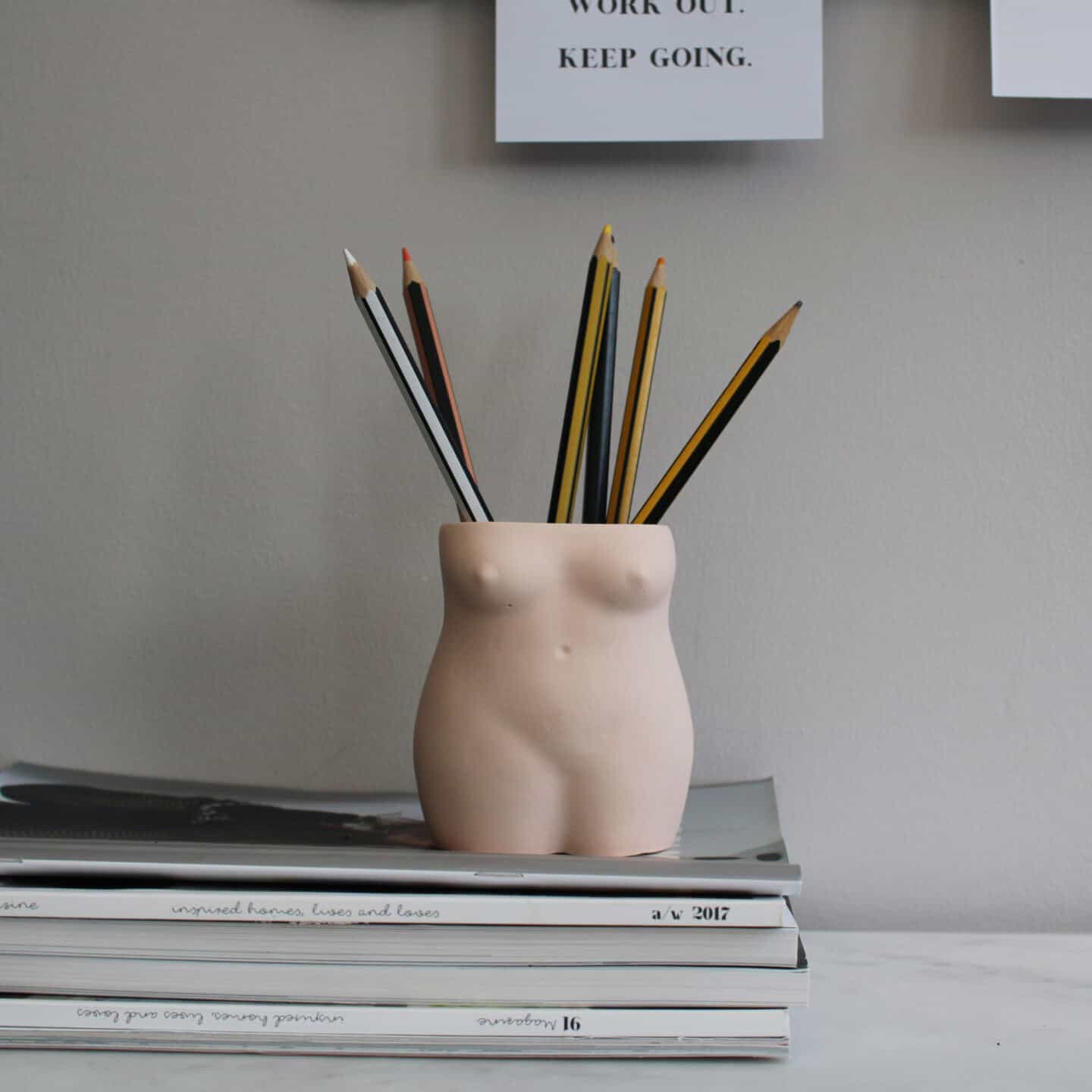 A pen pot in the shape of a woman's torso on a stack of magazines