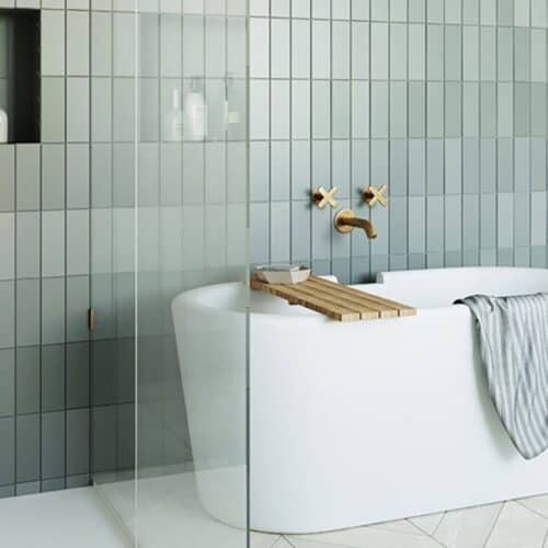 A free-standing bath in a bathroom with tiled green walls