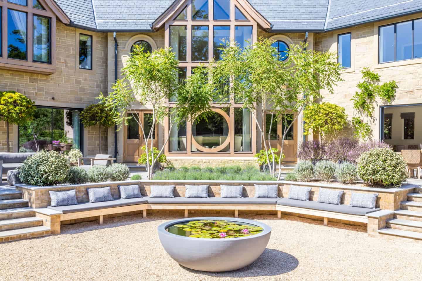 A modern home with some feature round windows a large curved bench seat in front and a water feature.