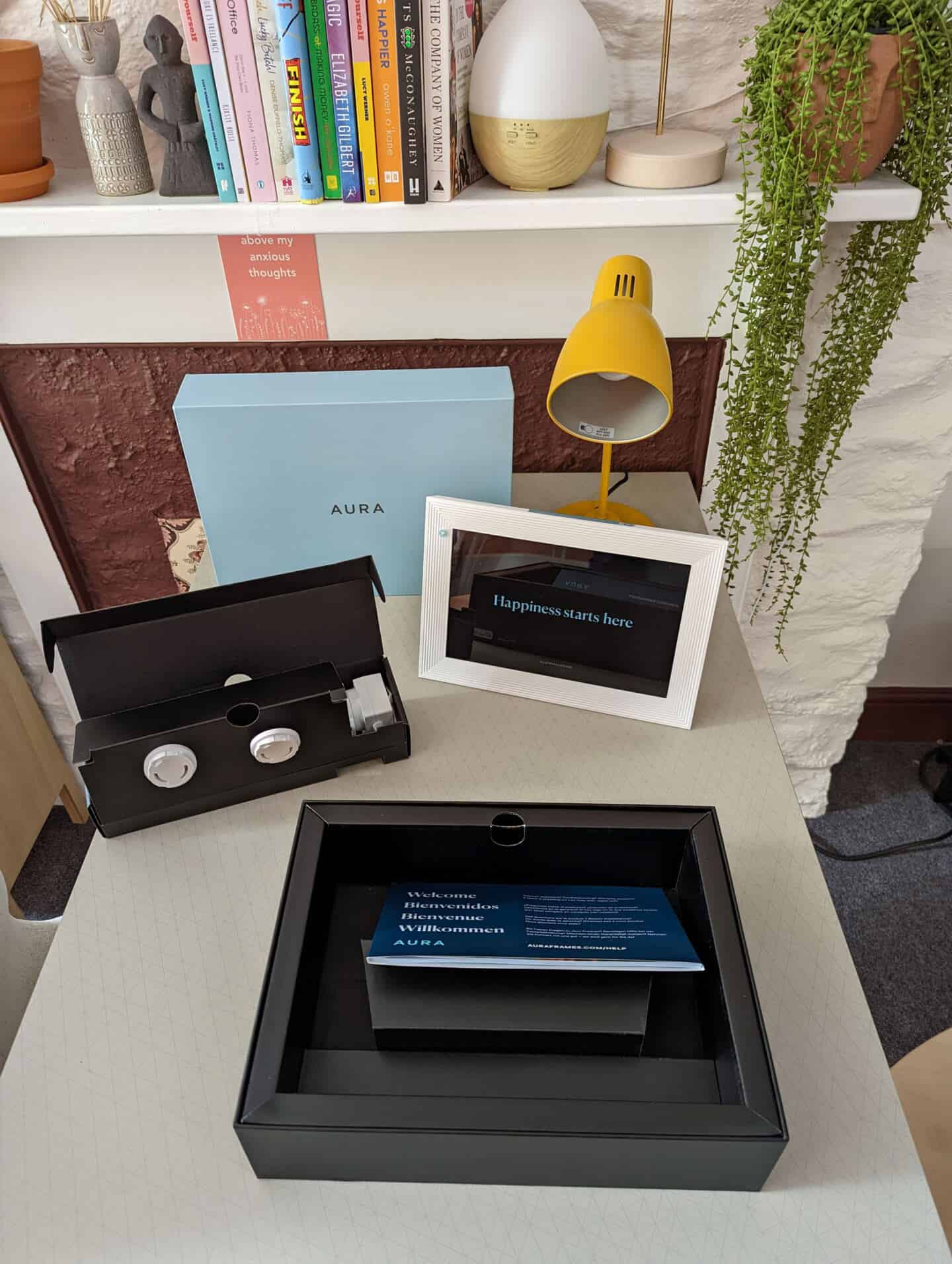 An open blue box on a desk next to a yellow lamp. A digital photo frame is on the desk next to all the power cables