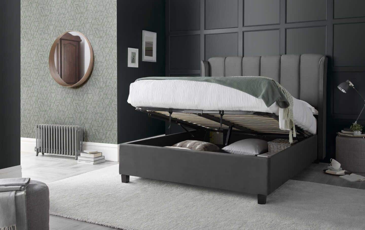 An open ottoman bed full of cushions in a grey bedroom with a panelled wall behind