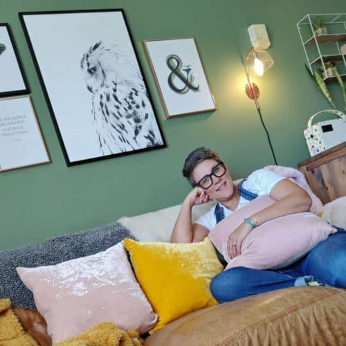 Woman sat on a leather sofa in a green room holding a pink cushion