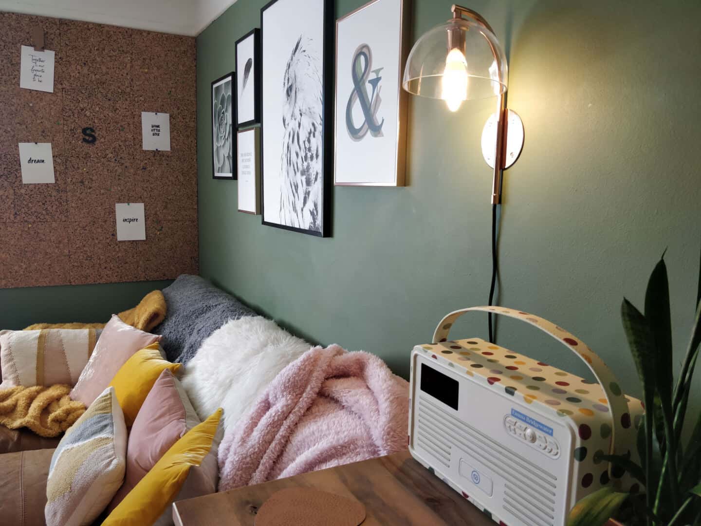 Autumn home updates with Habitat. A green living room featuring a brown leather sofa with a copper wall light and gallery wall above.