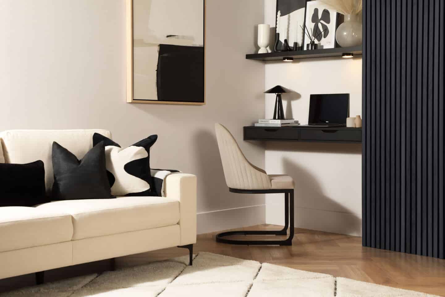 A sofa with black and white cushions on a white Berber rug with a small desk in nook beside