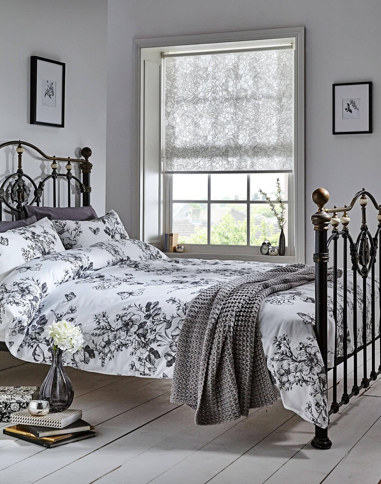 A bed with patterned bedding and a patterned roller blind on the window