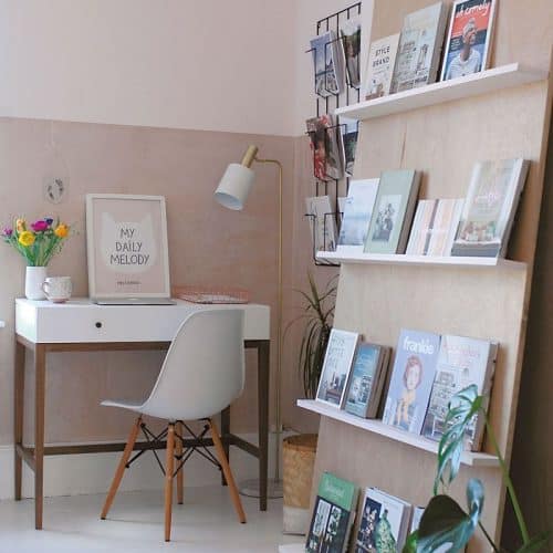 A small office space in the corner of a room uses leaning shelves to avoid damaging the wall