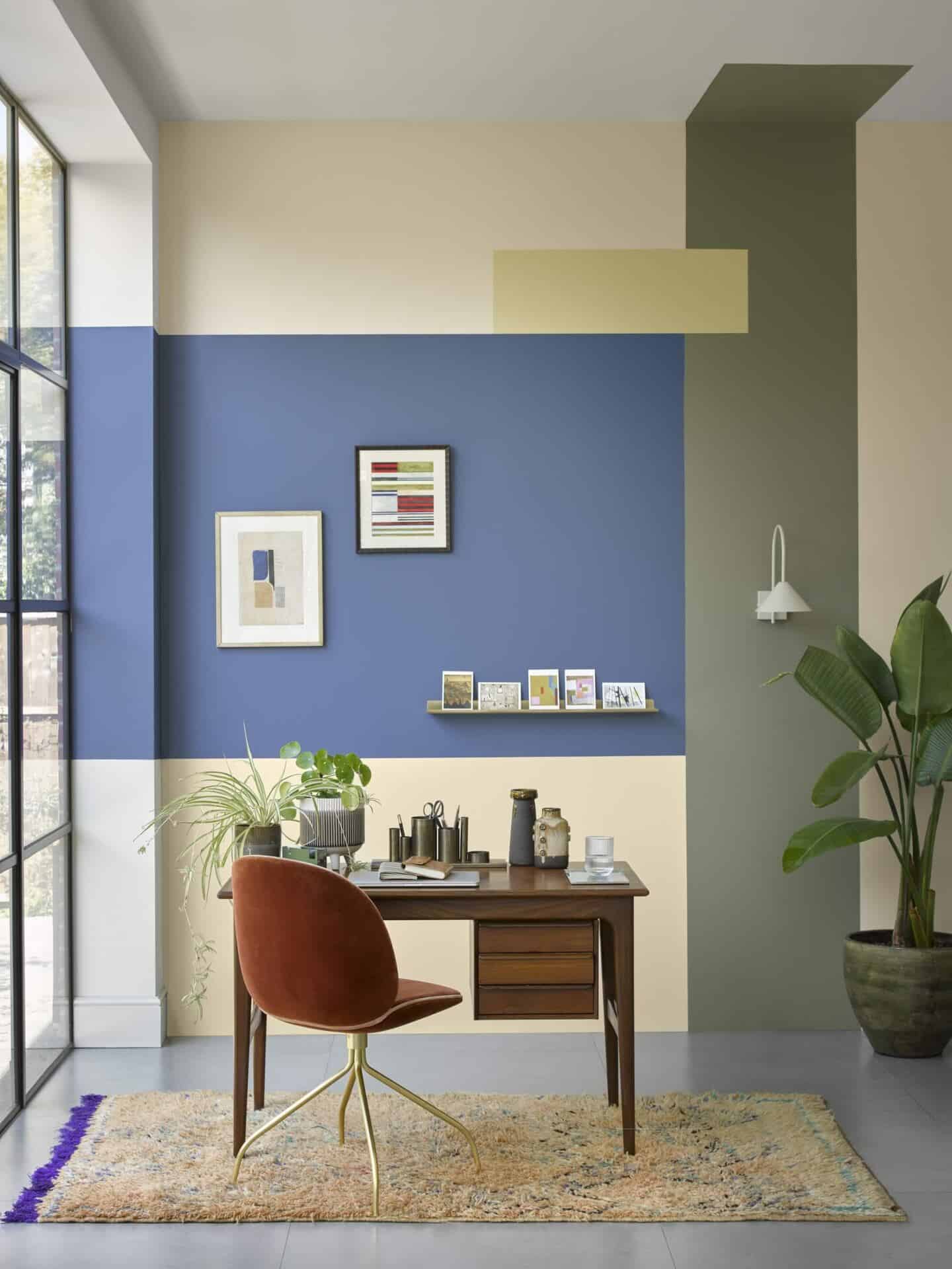 a desk beside floor to ceiling windows with geometric stripes painted on the walls in different colours