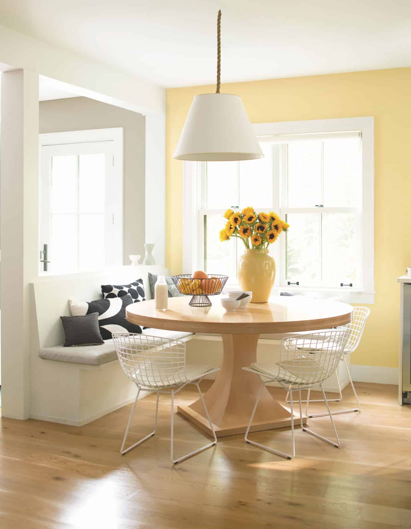 Pantone Colour of the Year 2021 - Illuminating. The colour psychology behind using yellow in interiors. A dining table in front of bench seating with a window behind. Wall painted in yellow paint from Benjamin Moore