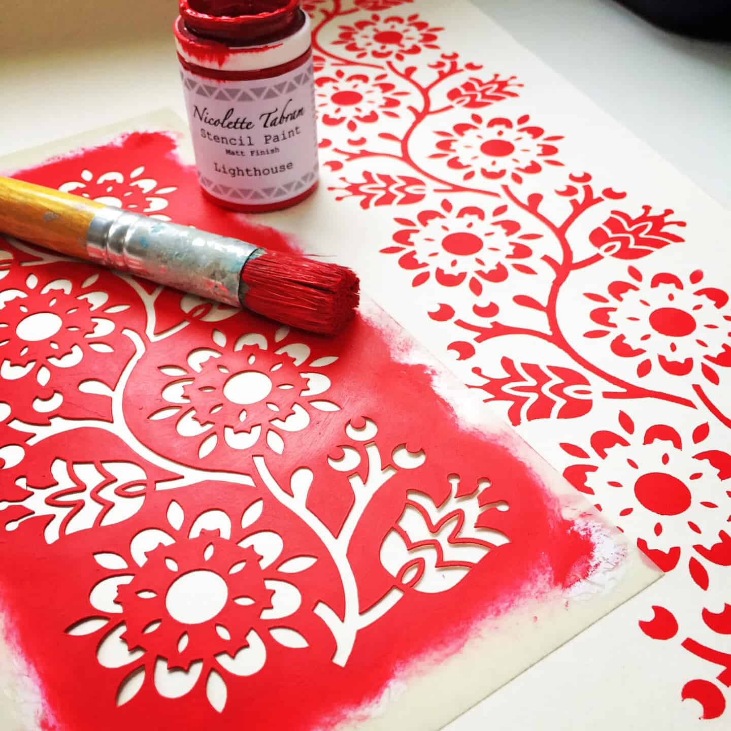 A floral stencil used for upcycling has been painted with red paint onto white fabric