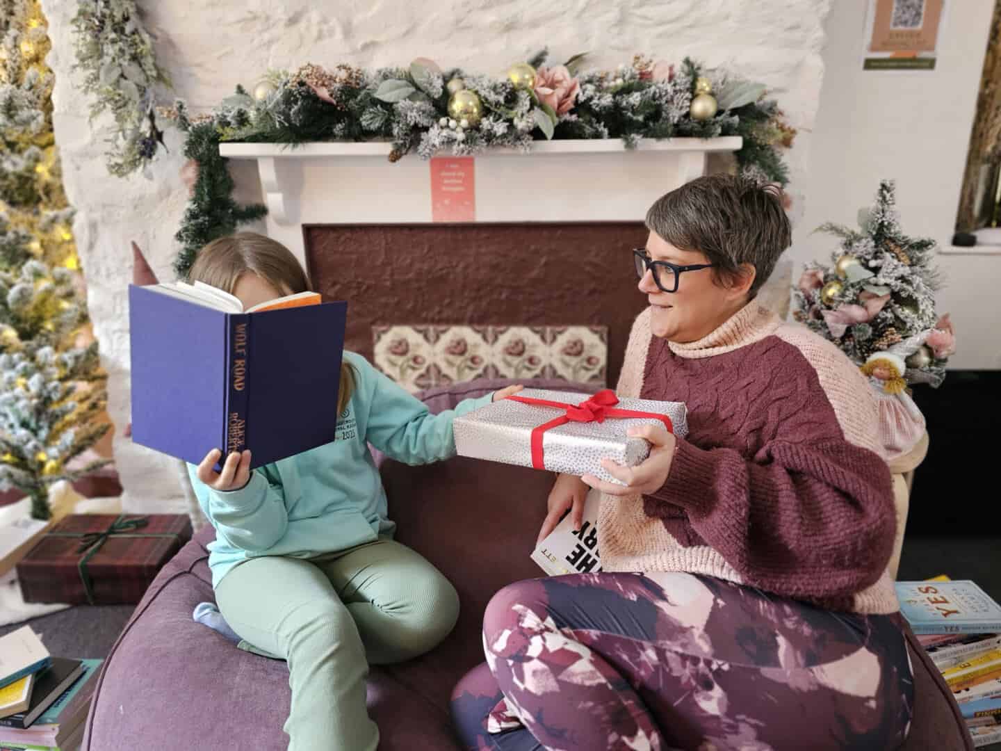 A child who is reading a book passes a Christmas gift to a woman in her forties