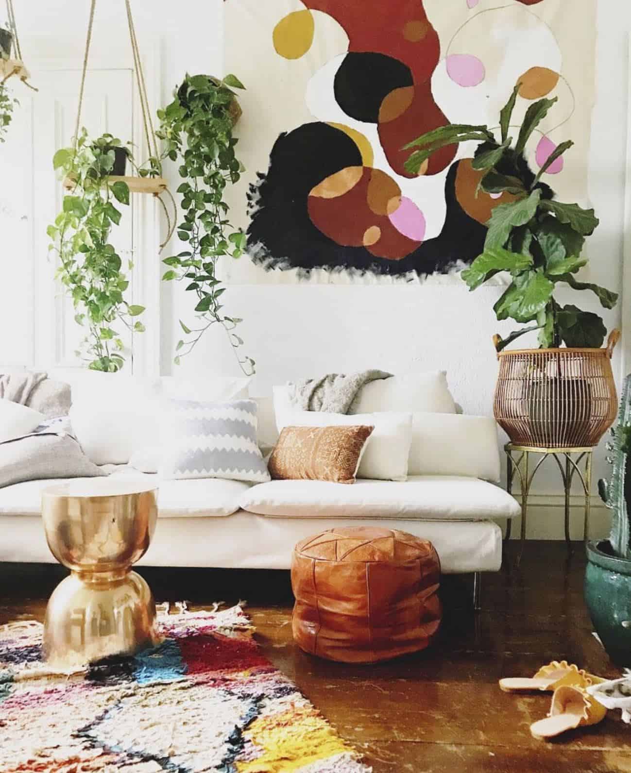 A bohemian style lounge featuring wall hangings, plants, leather Moroccan pouffes in earthy colours