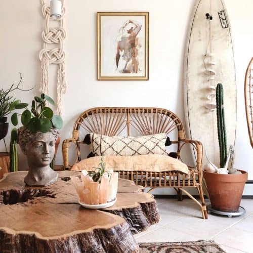 A bohemian style lounge featuring lots of natural materials, macrame wall hanging, terracotta pots and a surf board