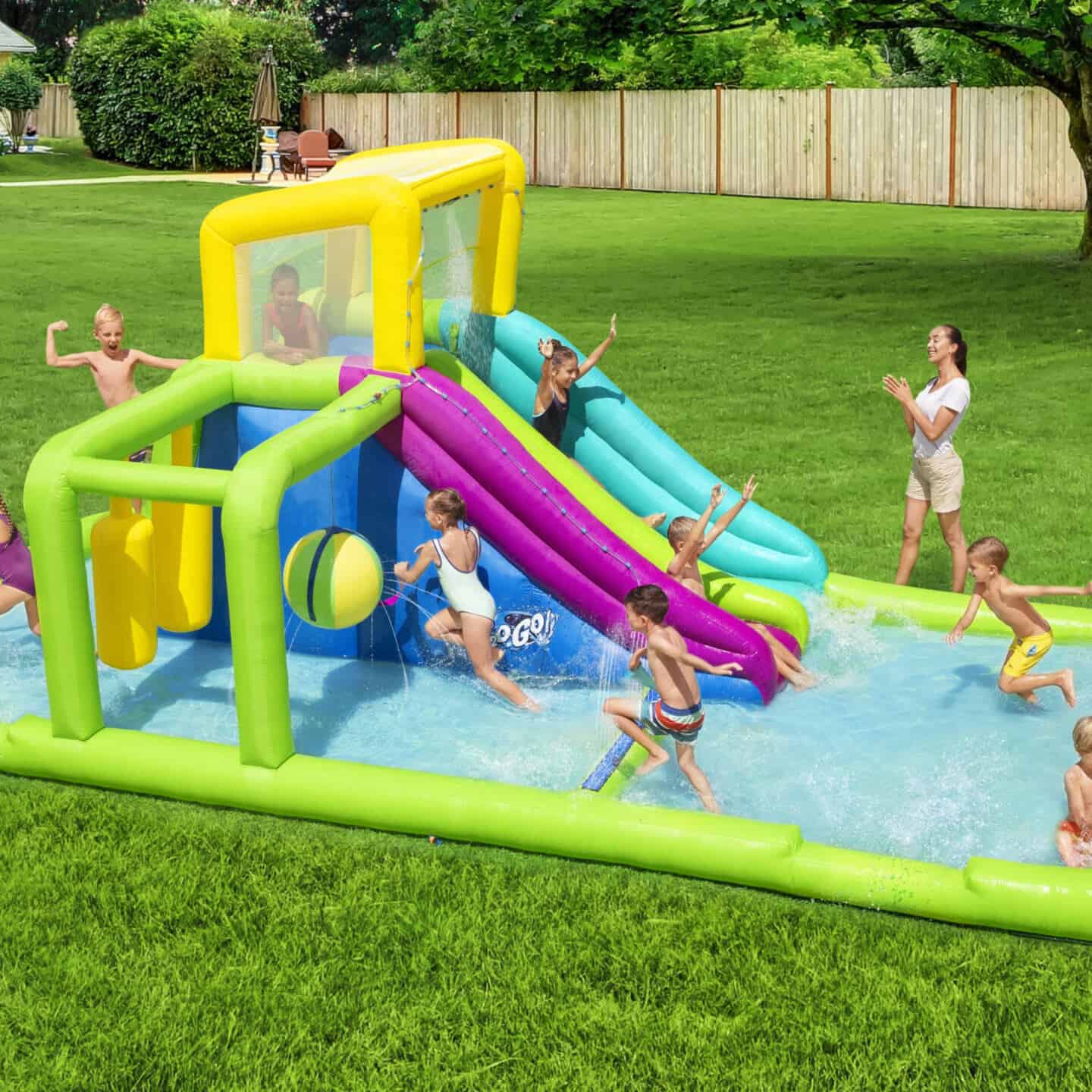 Kids enjoying an inflatable splash pad in a large garden