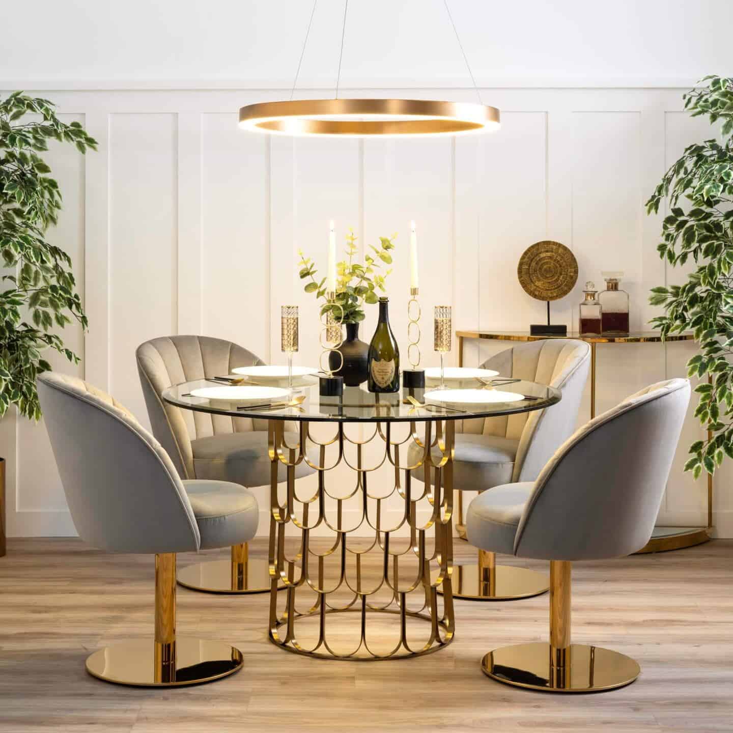 An LED pendant light suspended above a glass and brass dining table with four grey velvet chairs around it