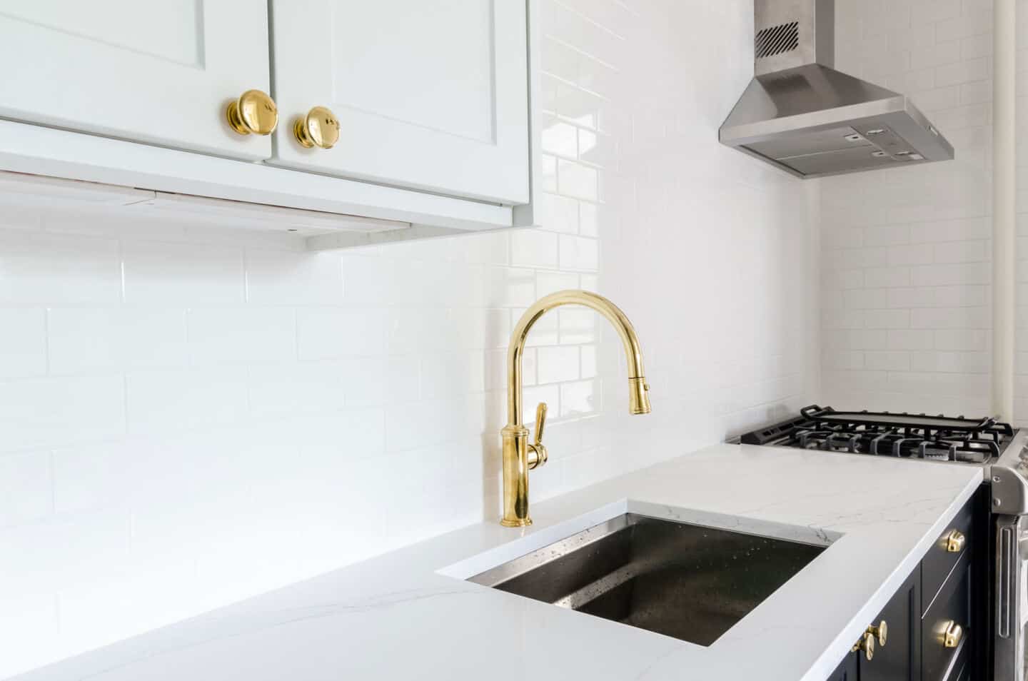 6 Easy Ways to Spruce Up Your Kitchen on a Budget - replace the tap. Image of a brass tap on a white countertop with white wall tiles behind.