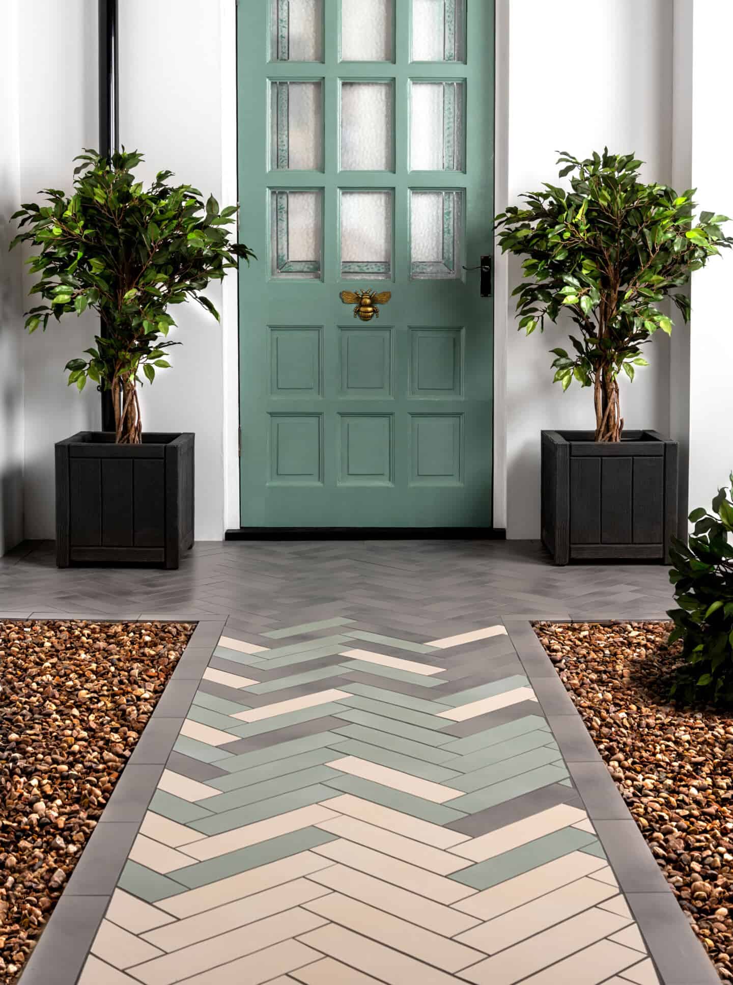 A sage green front door with bumblebee knocker. A potted tree is on either side and there is a tiled path leading up to it for maximum curb appeal