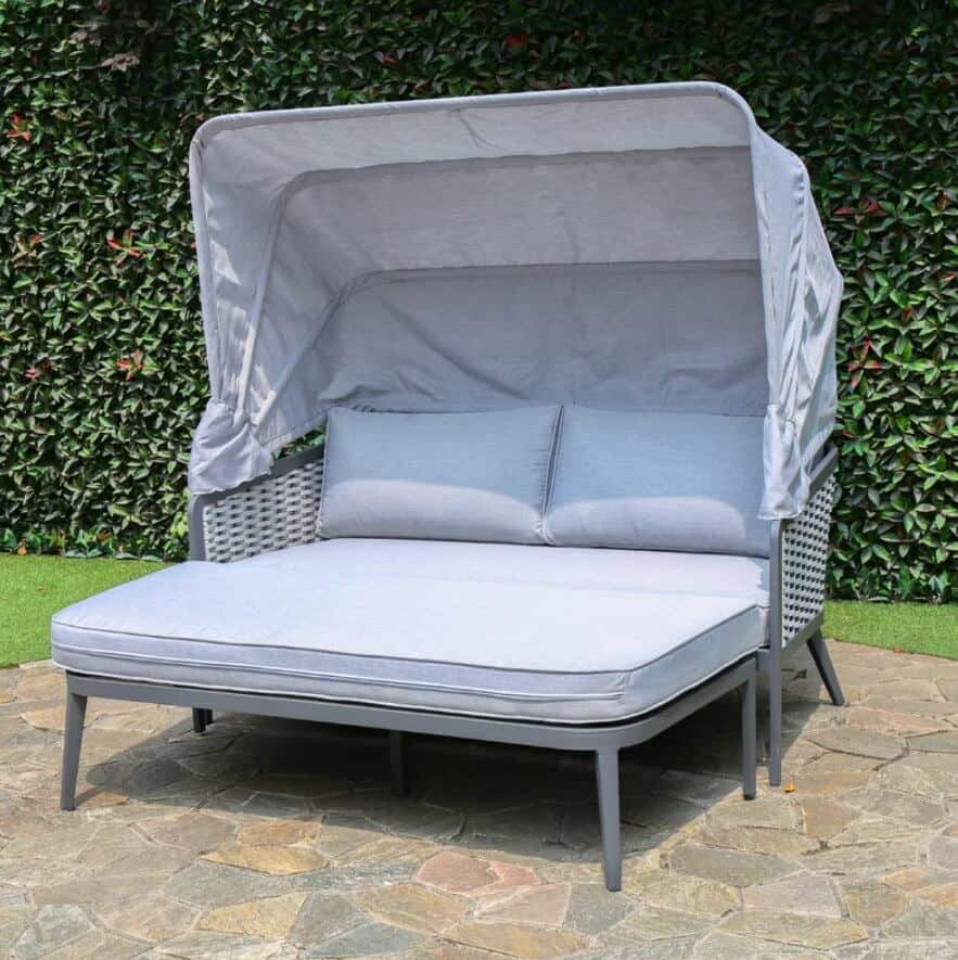 a garden daybed with shade canopy on a patio with bushes behind