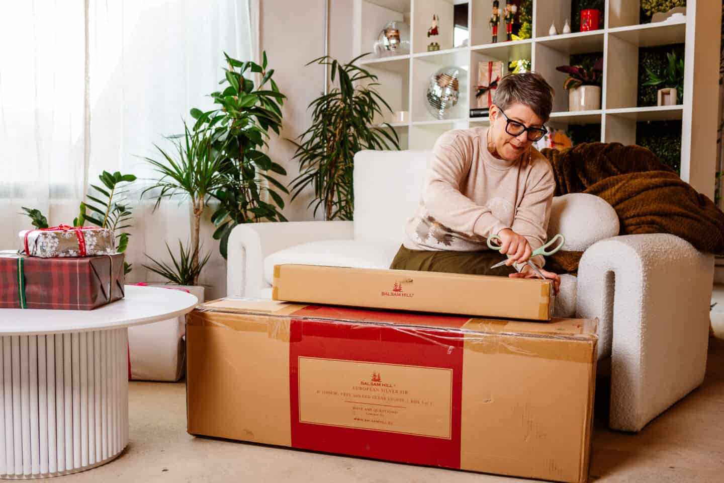 A woman in her forties sat on a sofa  unpacking realistic Christmas decorations from Balsam Hill 