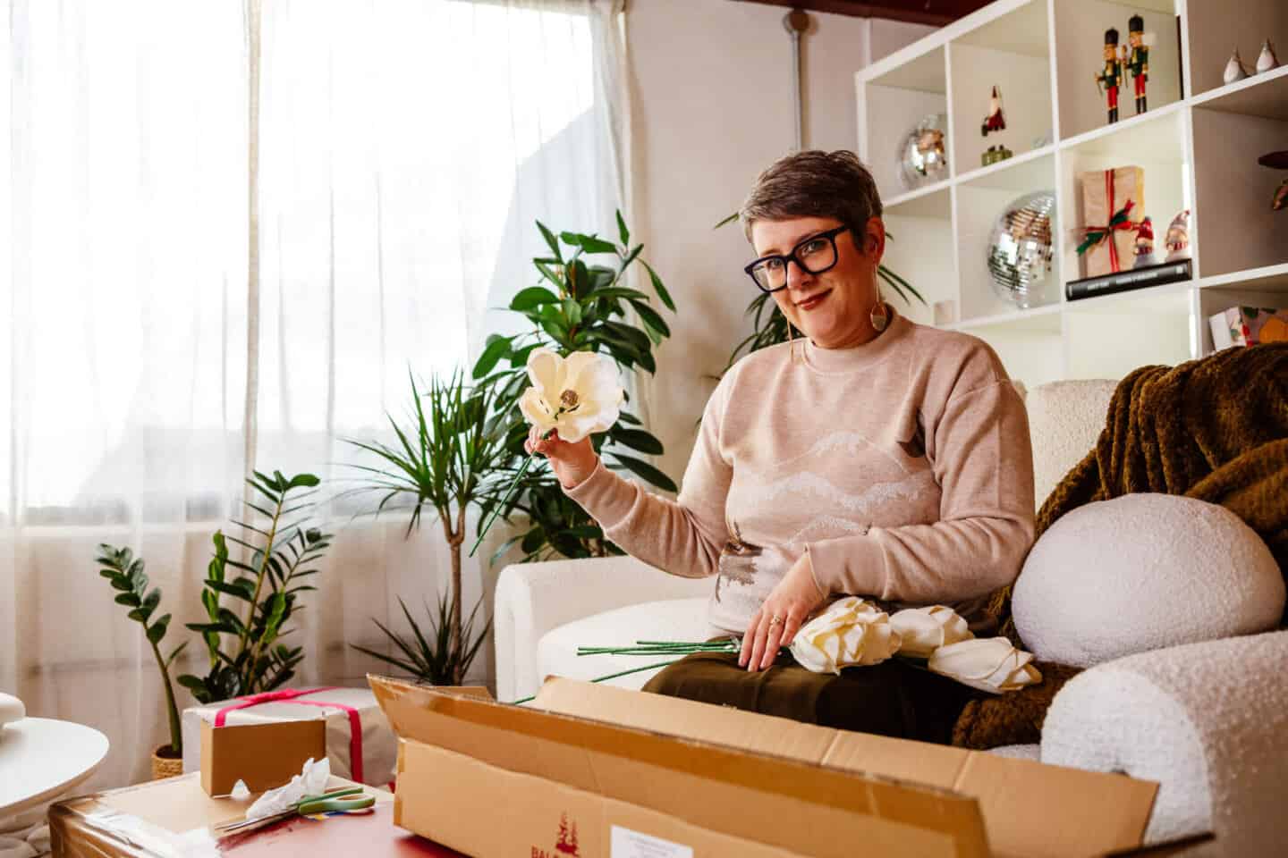 A woman in her forties sits on a sofa and unpacks some tree picks from Balsam Hill