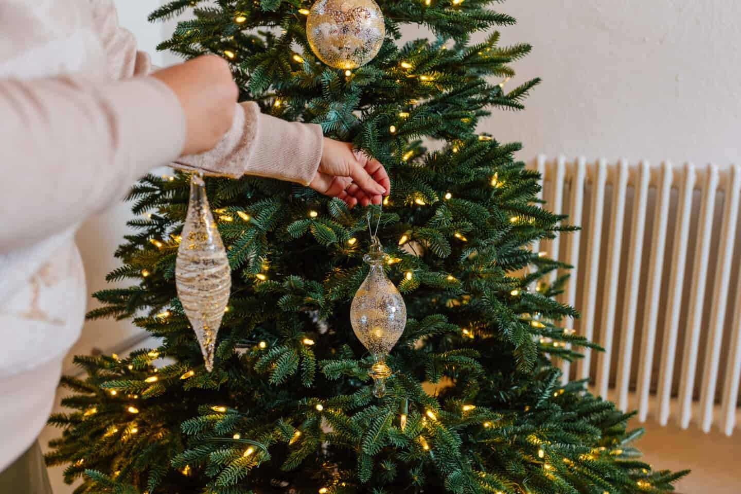 A woman in her forties hangs Christmas baubles on a realistic artificial Christmas tree from Balsam Hill 