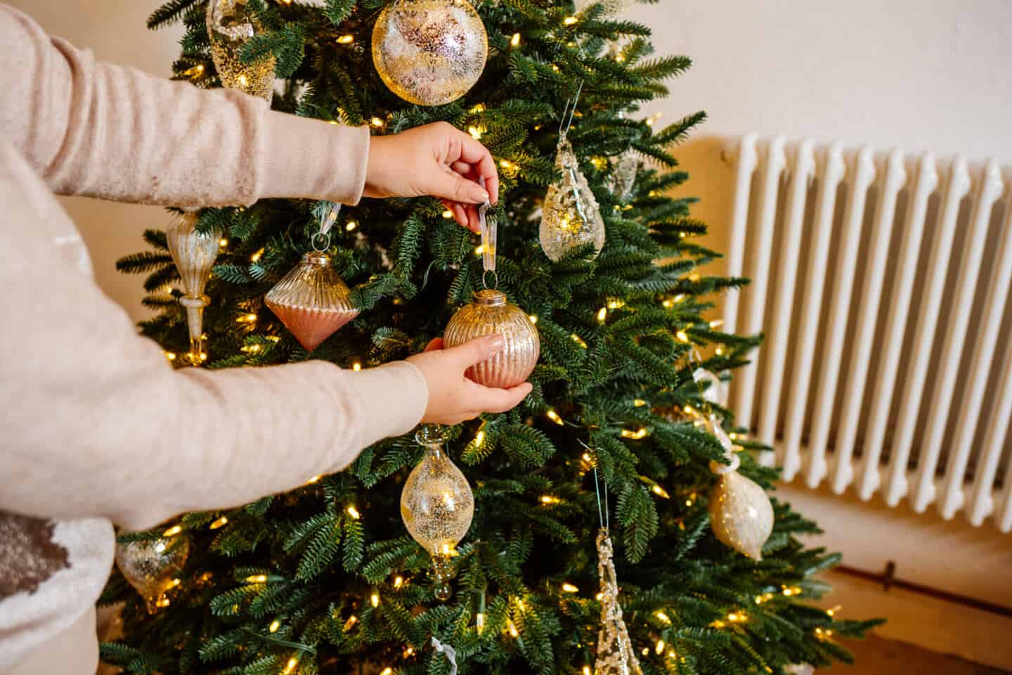 A woman in her forties hangs Christmas baubles on a realistic artificial Christmas tree from Balsam Hill 