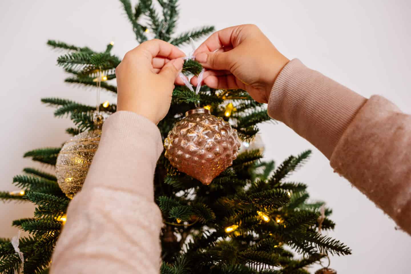 Two hands hand a Christmas bauble from Balsam hill on an artificial Christmas tree