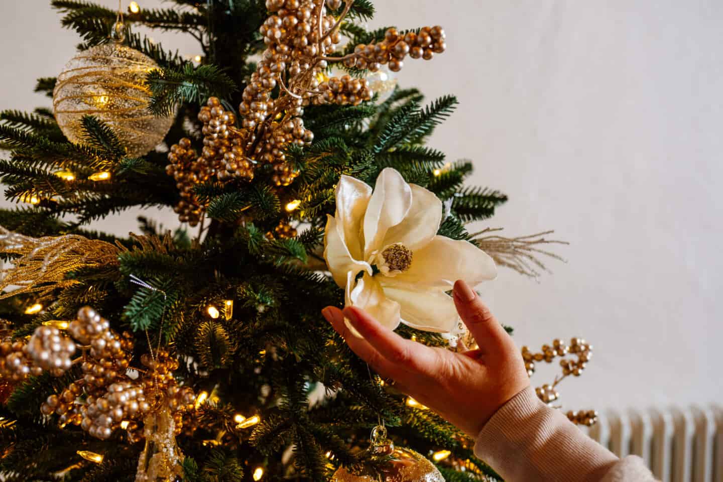 A woman's hand holds a Christmas tree pick on a realistic artificial Christmas tree from Balsam Hill 