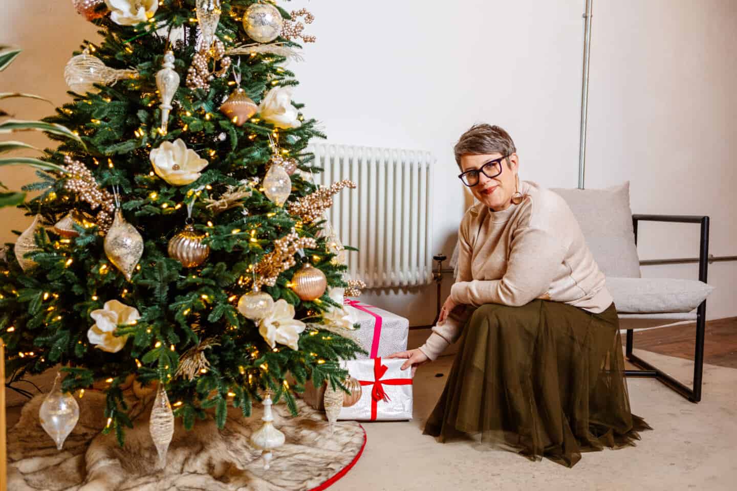 A woman in her forties places  Christmas presents beneath a realistic artificial Christmas tree from Balsam Hill 