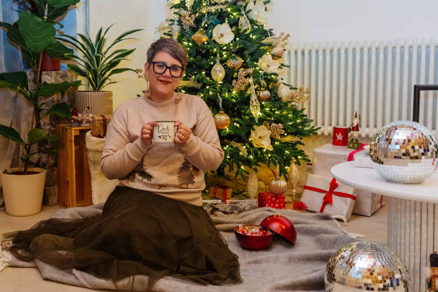 A woman in her forties sat on the floor with a realistic artificial Christmas tree from Balsam Hill in the background