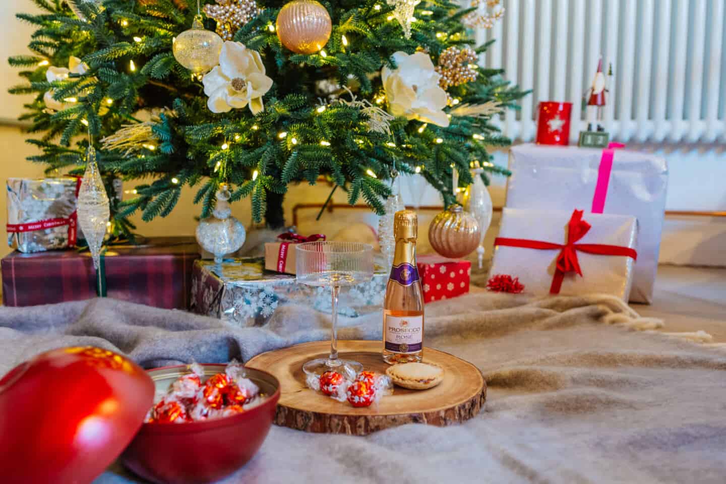 Prosecco, a mince pie and Lindor chocolates on a blanket in front of an artificial Christmas tree from Balsam Hill