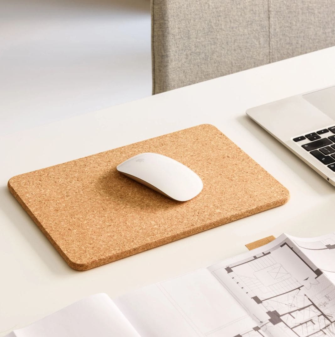 A cork mouse mat on a desk next to a laptop