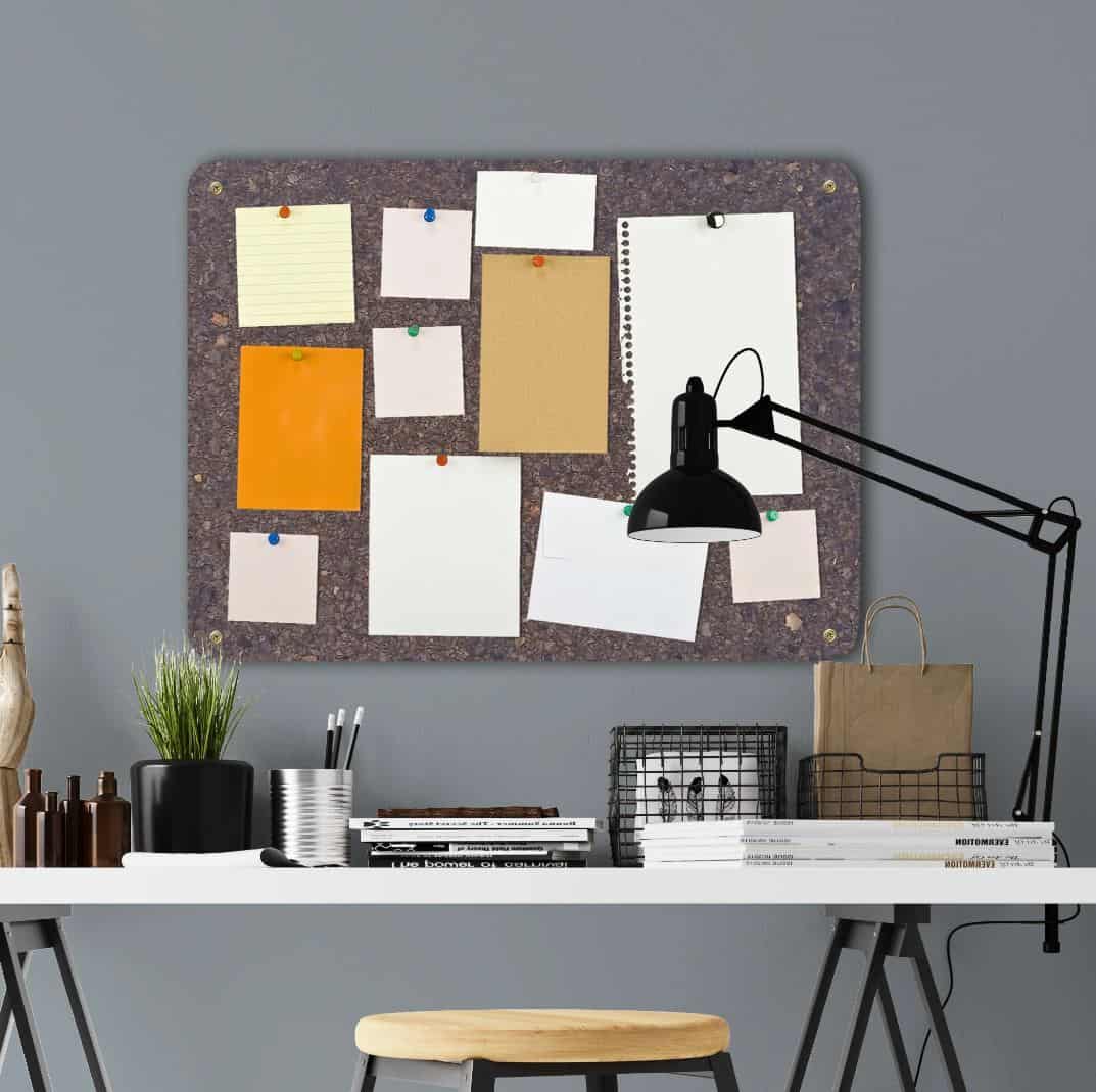 A desk with a cork pin board hanging above covered in pinned up paper