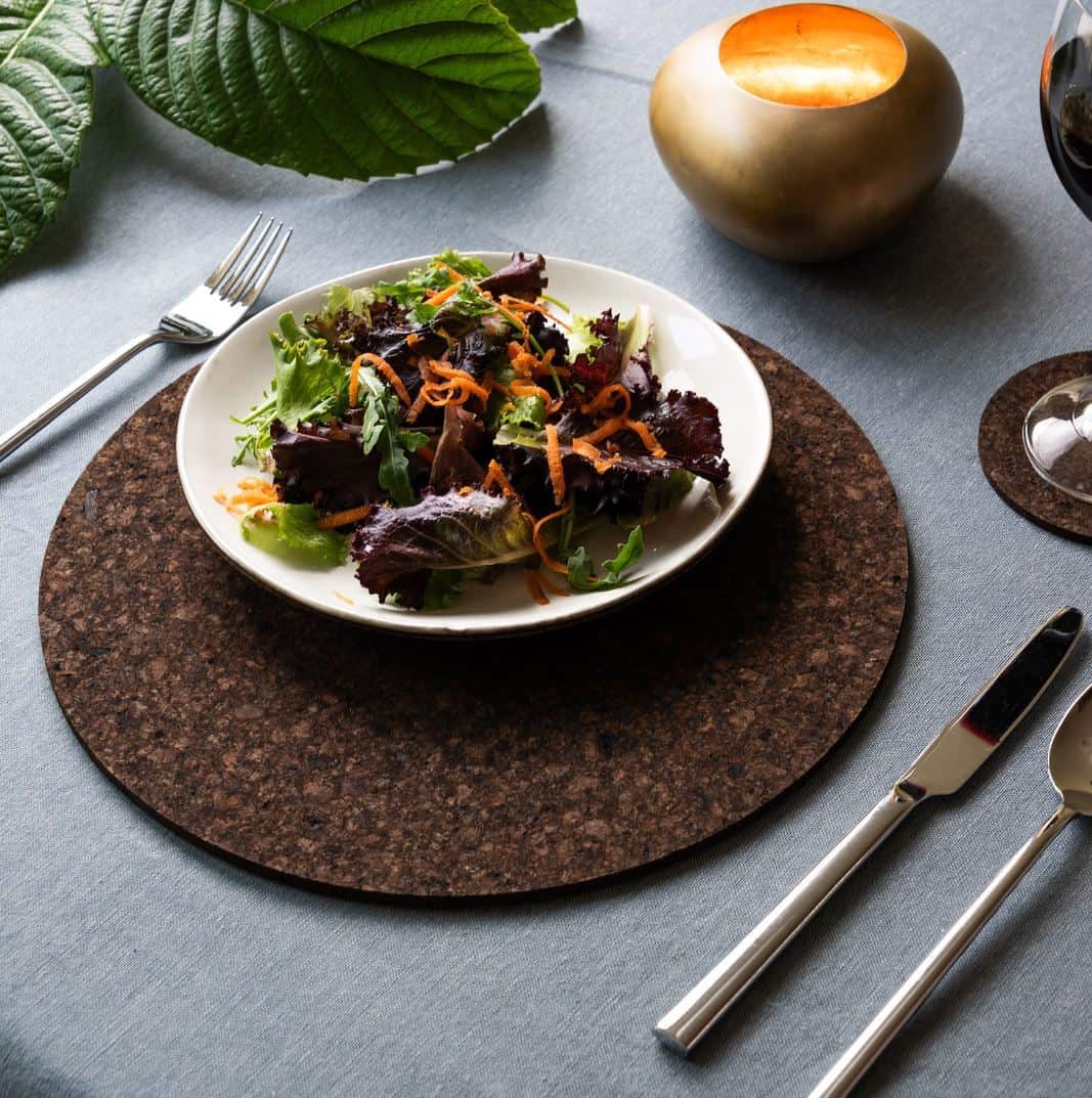 A bowl of salad on a cork placemat on the dining table