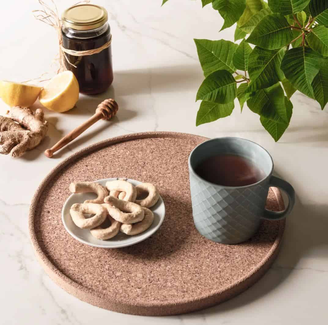 A cup of tea and a place of biscuits on a cork tray