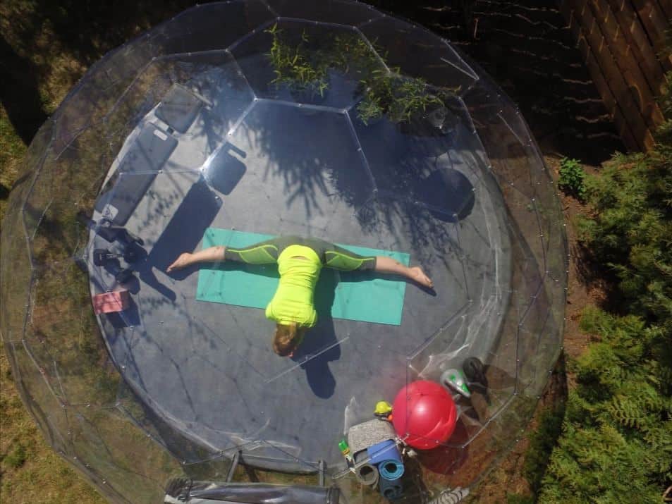 A women with her legs spread in the splits on a yoga mat inside a garden igloo