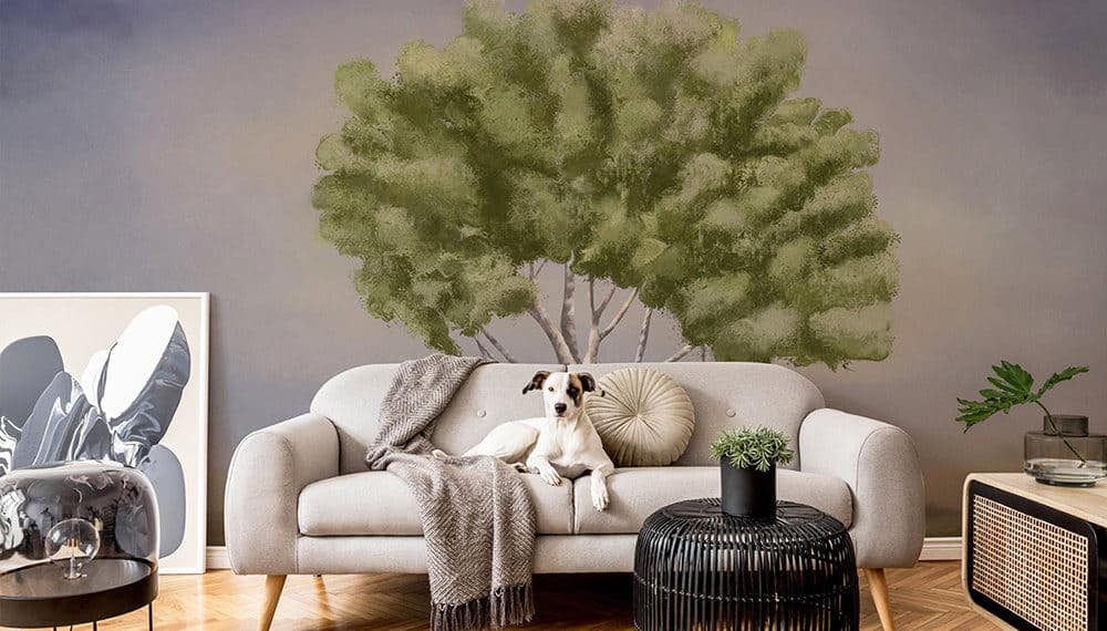 A small dog sat on a sofa in front of wall featuring a tree wall mural