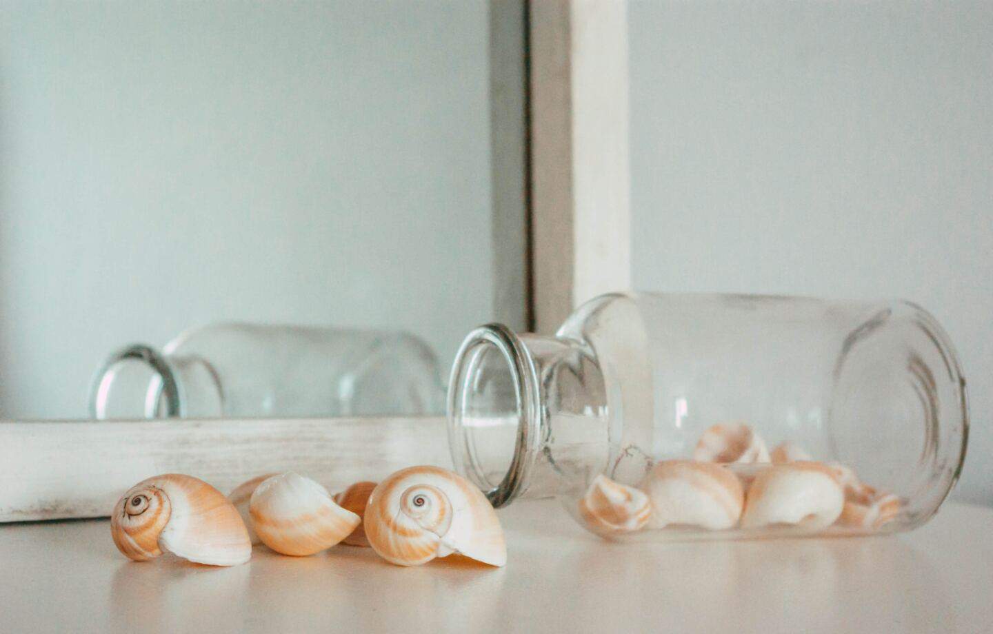 Shells spilling out of a small glass bottle in front of a mirror on a mantlepiece