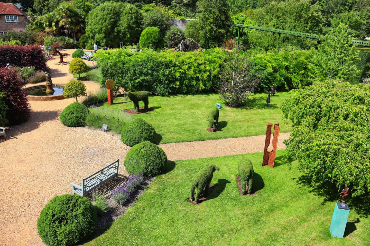 a large garden with gravelled paths, well trimmed bushes, water features and animals carved from bushes