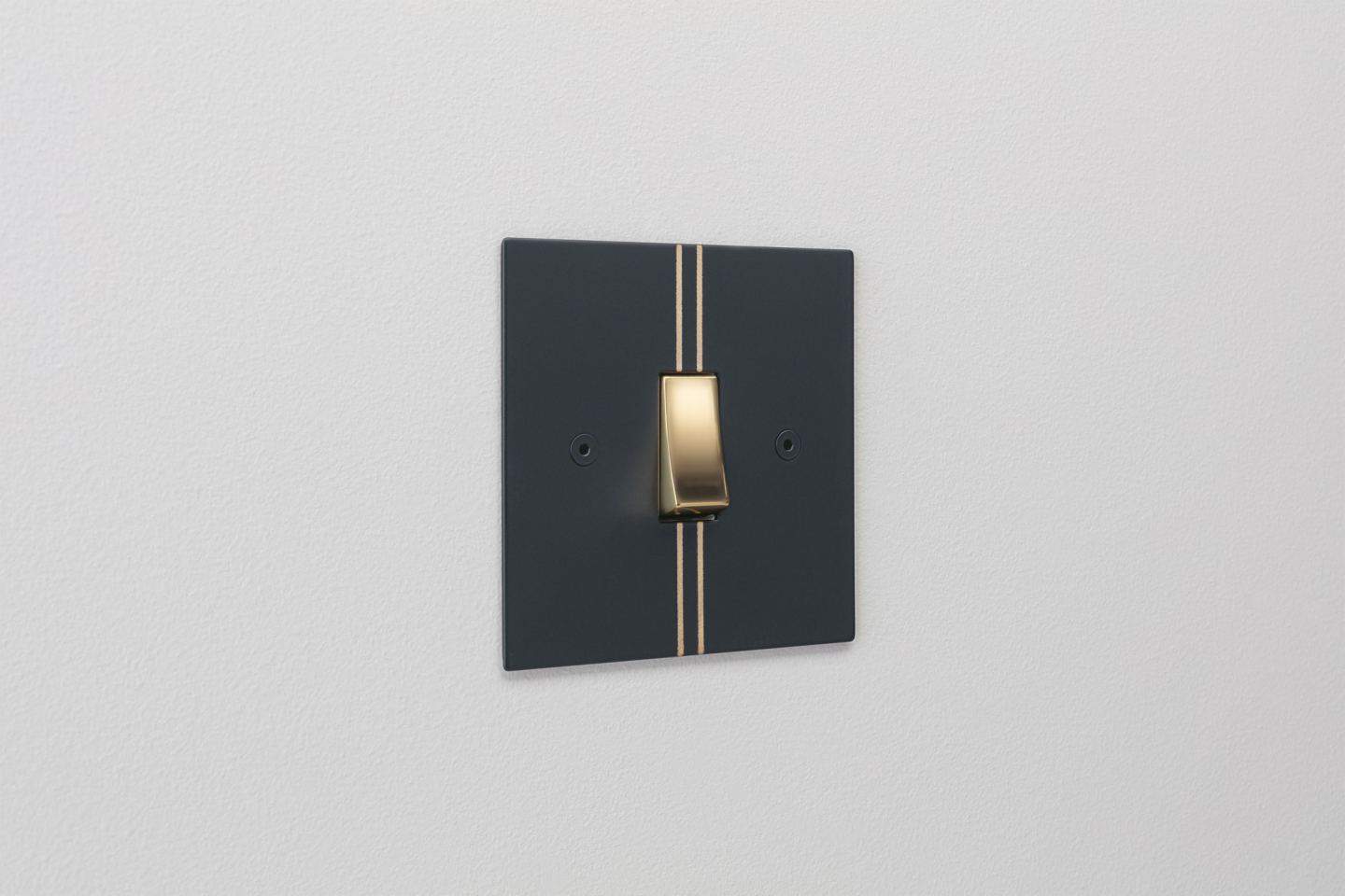 Designer light switches by Kelly Hoppen for Focus SB. Pinstripe is a matt black switch plate featuring two metallic gold pinstripes and a gold switch. 