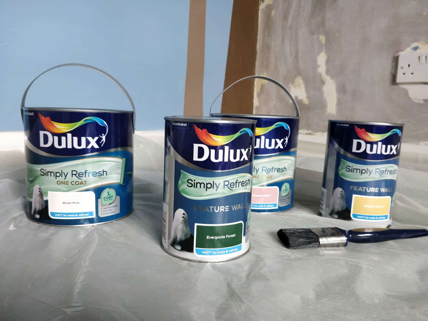 Dulux Simply Refresh paint cans on a plastic cover with a paintbrush. These colours will be used to create a DIY Painted Arch Accent Wall