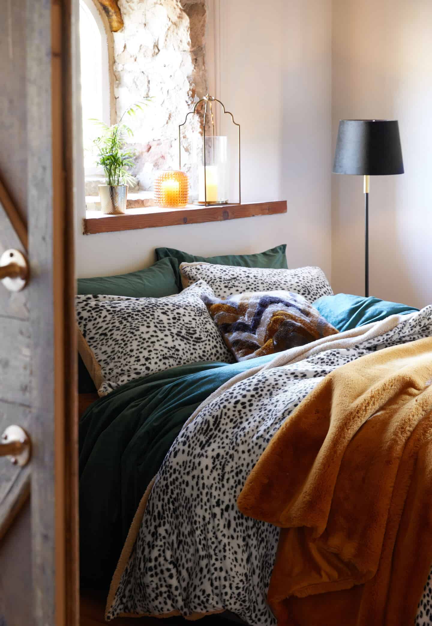 A bed below a window dressed in teddy bear fluffy aninmal print bedding