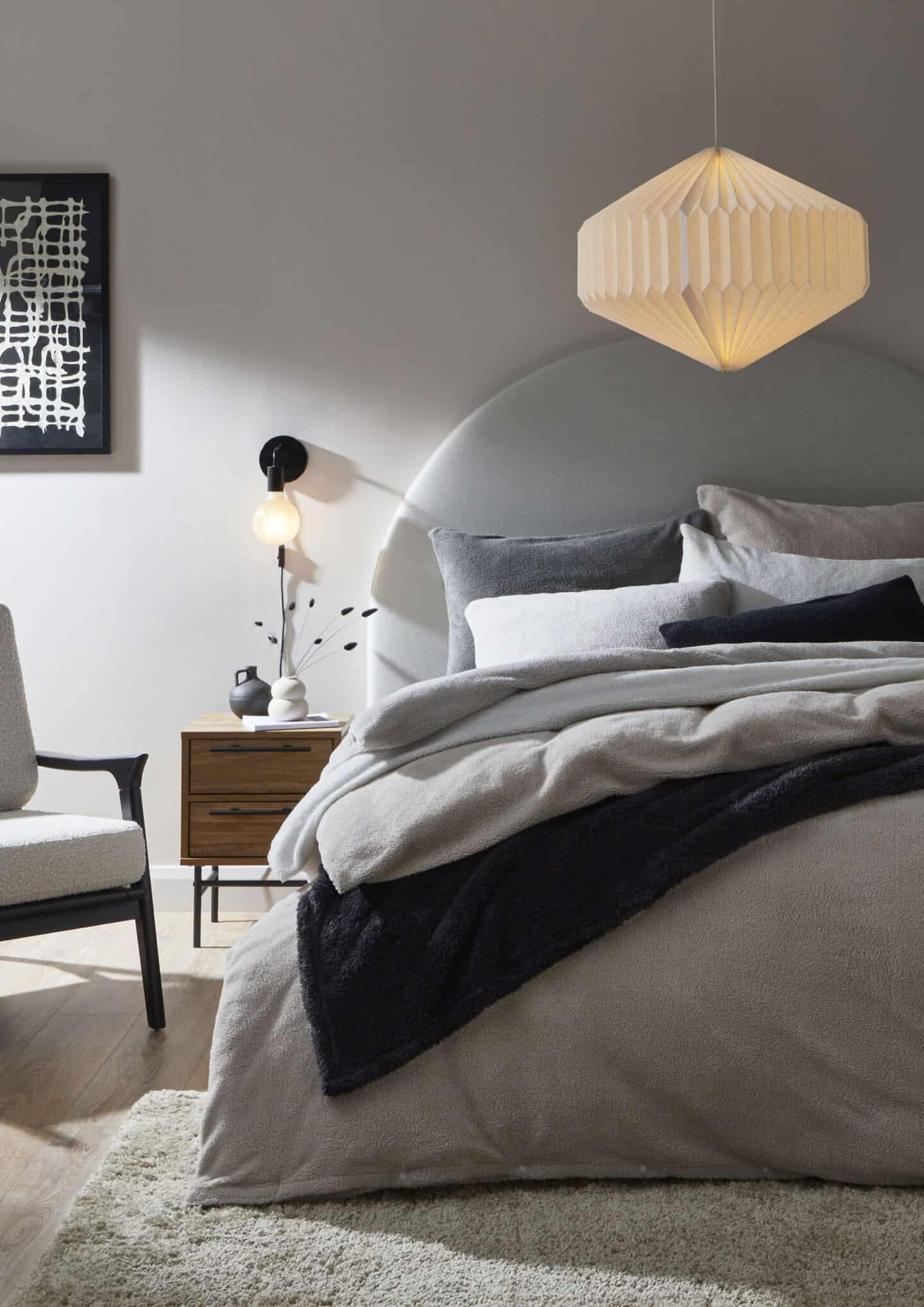 A minimal Scandi style bedroom with a bed dressed in layers of grey teddy bear bedding