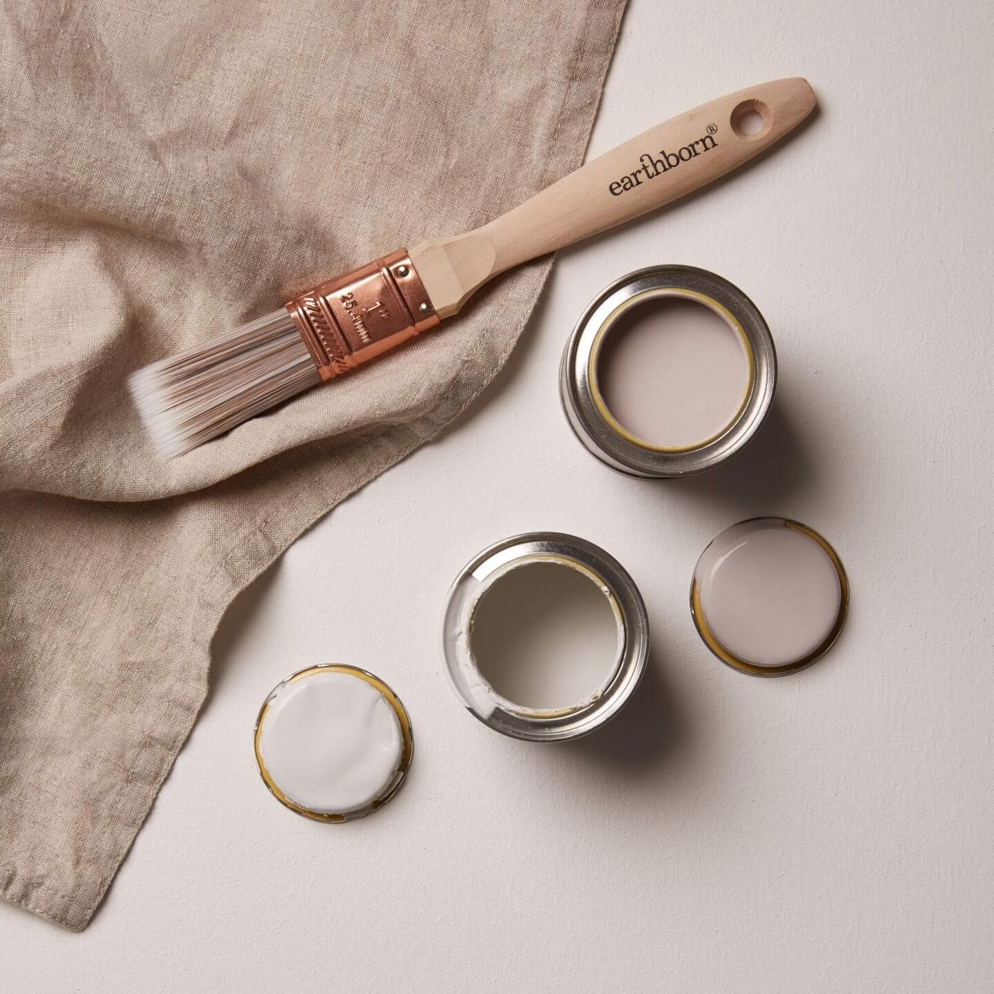 two open tester paint pots with a linen napkin and a paintbrush nearby