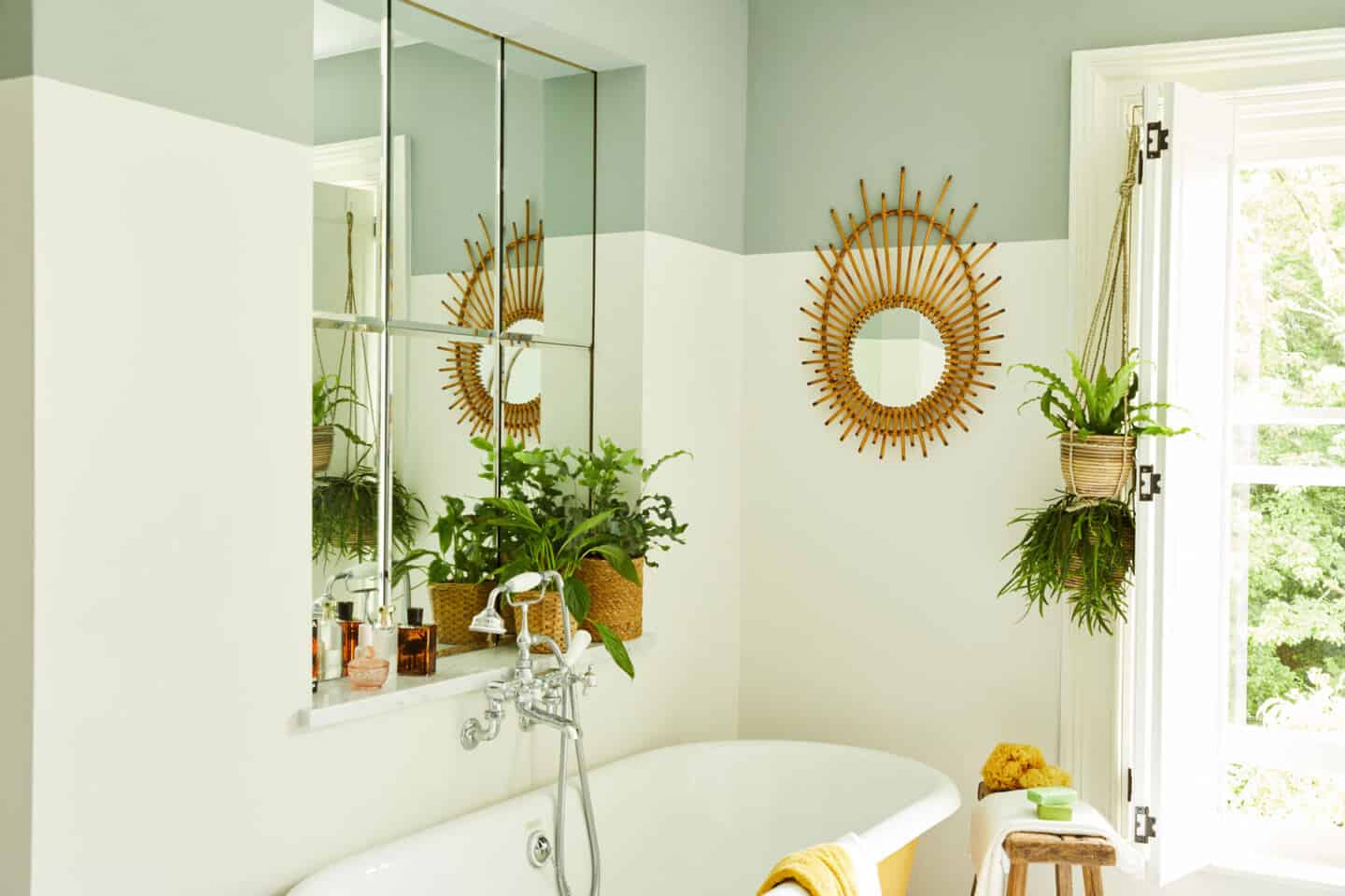 A bright an airy bathroom with a freestanding yellow tub and lots of plants. The lower wall is painted in white and the upper wall is painted green.